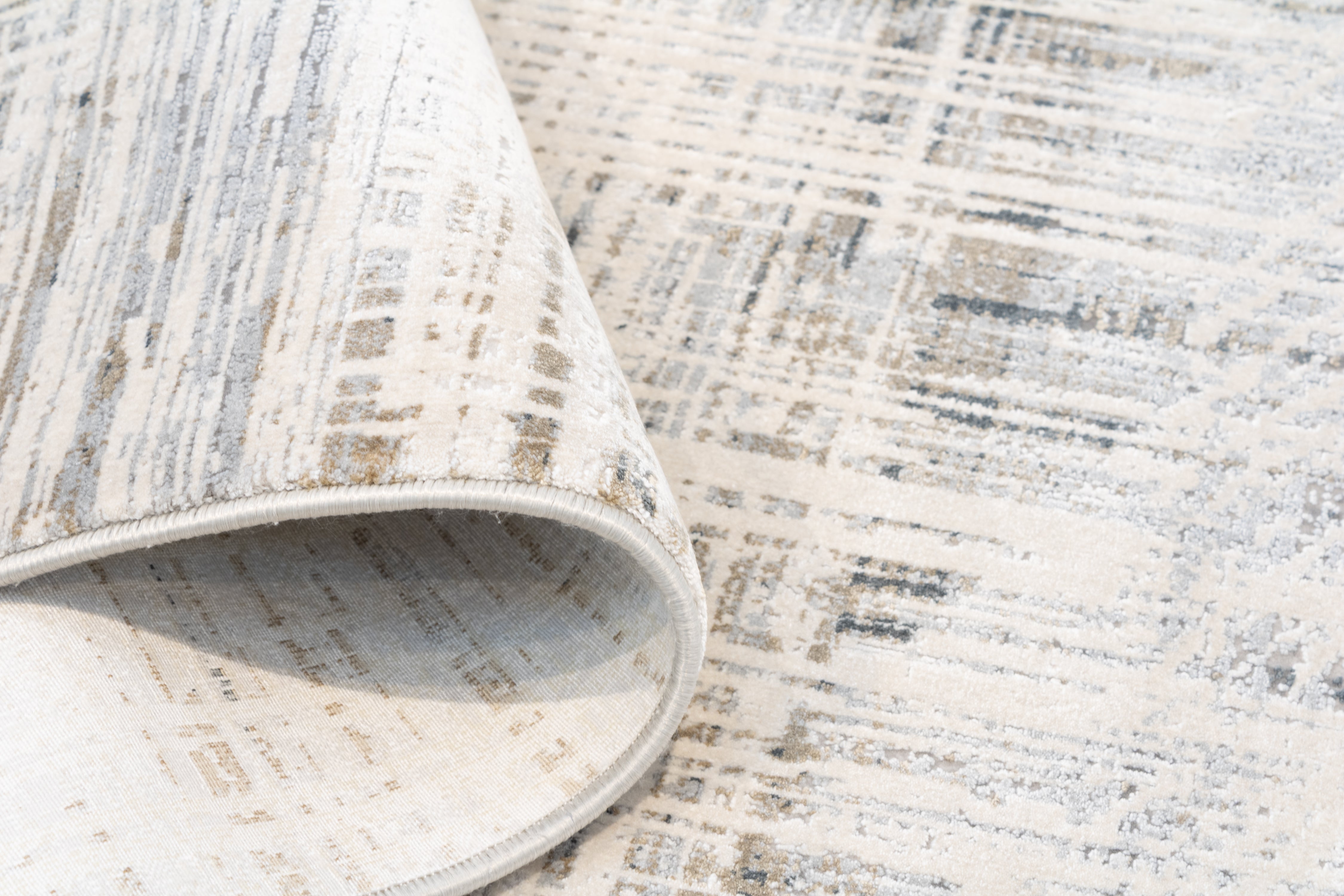Corner of the Hampton bamboo silk rug folded back to reveal the low pile surface and woven backing, with the abstract ivory, slate, and taupe pattern visible on the face