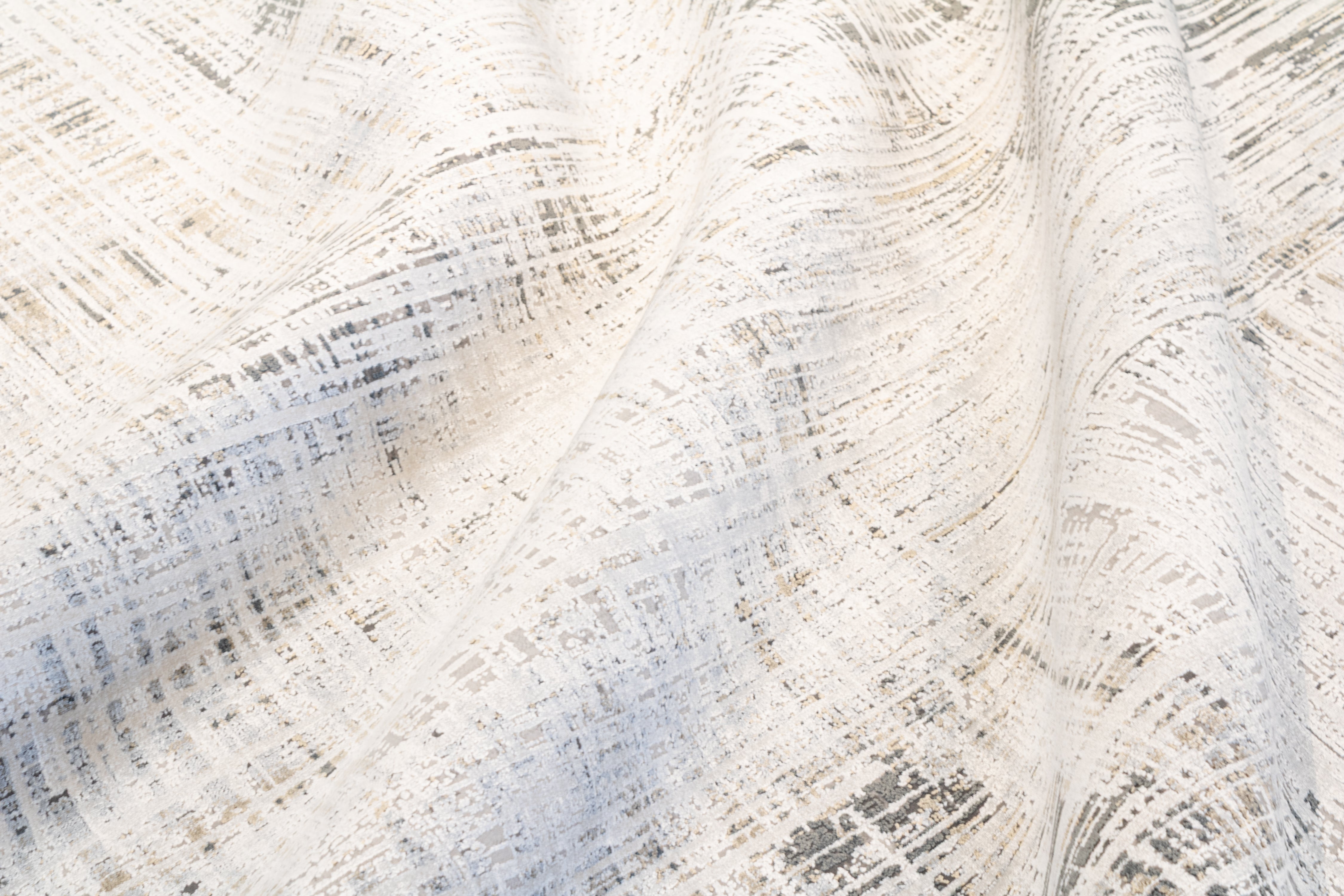 Close-up of the Hampton bamboo silk rug draped in soft folds, revealing the silky luster of the pile, the flowing movement of the abstract crosshatch pattern, and the cool blue and warm taupe tones across the ivory field