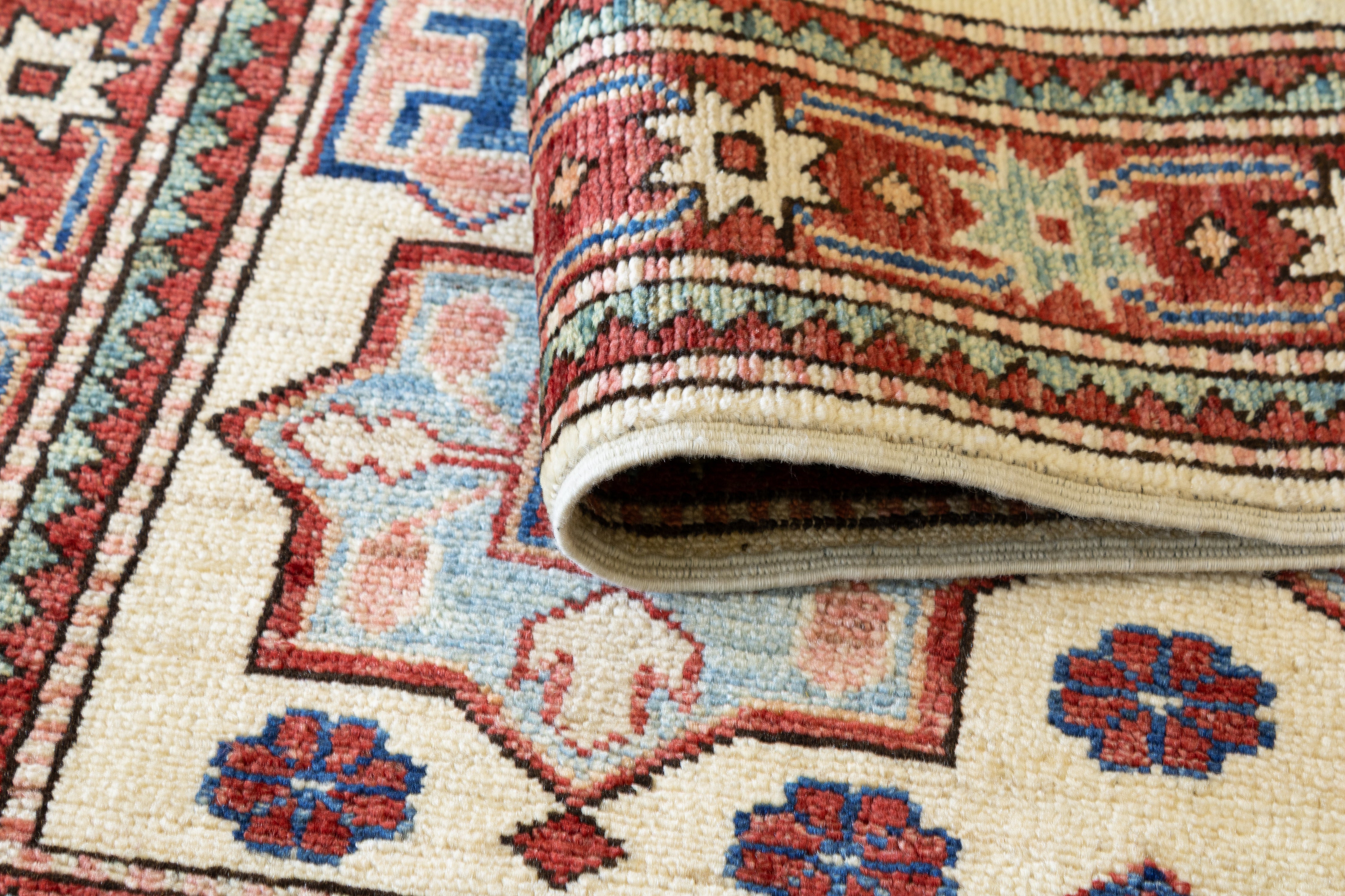 Hand-knotted ivory wool Pakistan Kazak rug with a navy diamond medallion, tribal geometric field motifs including a woven figure, and a terracotta star border, 2'8" x 4'.