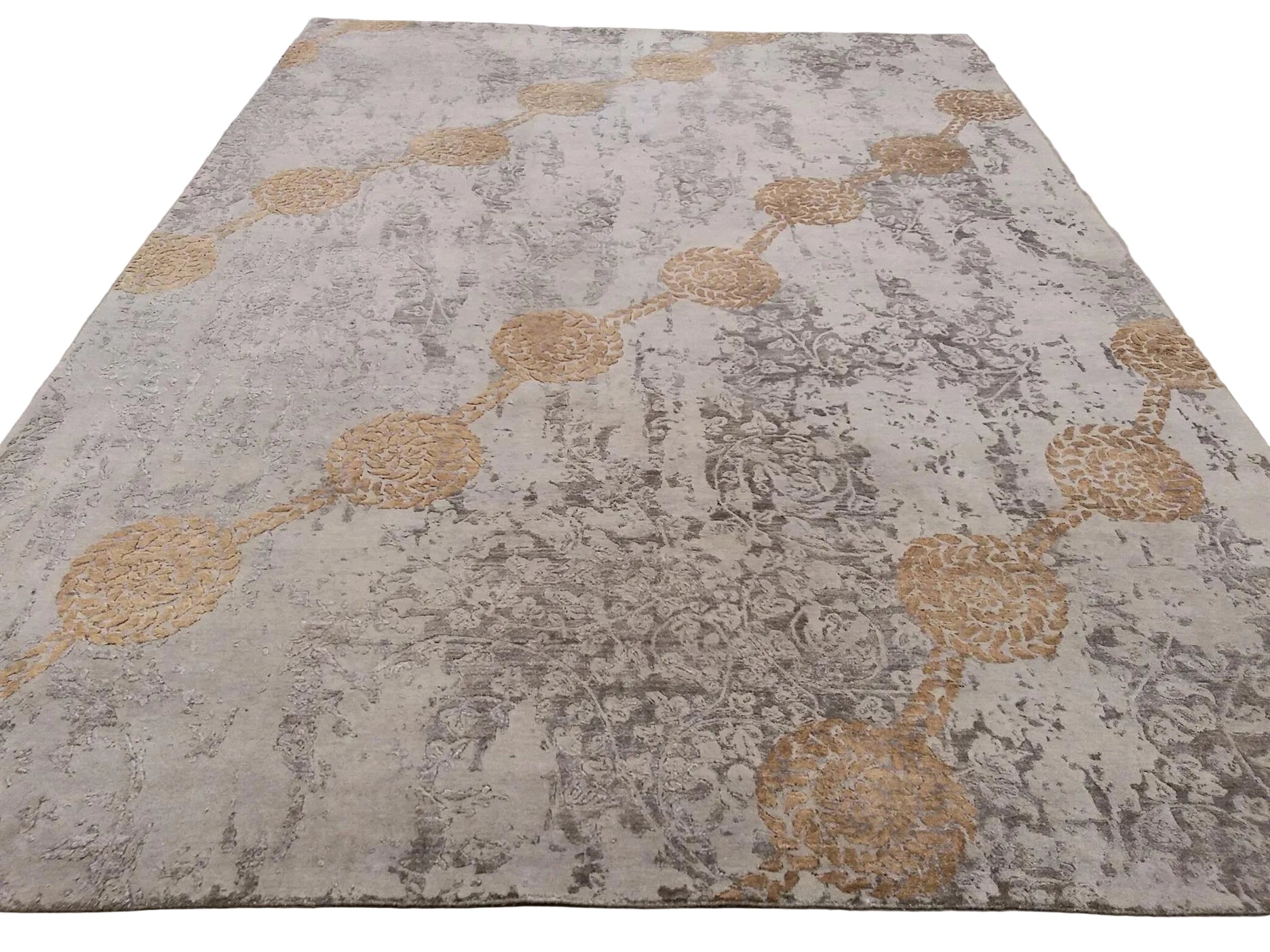 A large rectangular area rug laid flat on a concrete floor, featuring a distressed abstract pattern in beige, gray, and muted gold with circular medallion motifs.