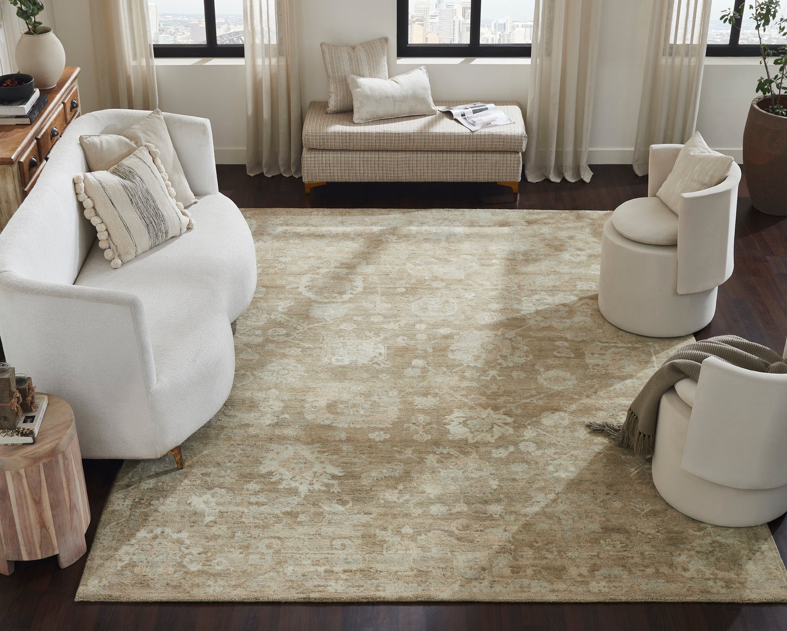 The Remus hand-knotted wool rug anchoring a modern living room with white bouclé seating, a houndstooth bench, and dark hardwood floors, demonstrating its scale and warm neutral colorway in a layered interior setting