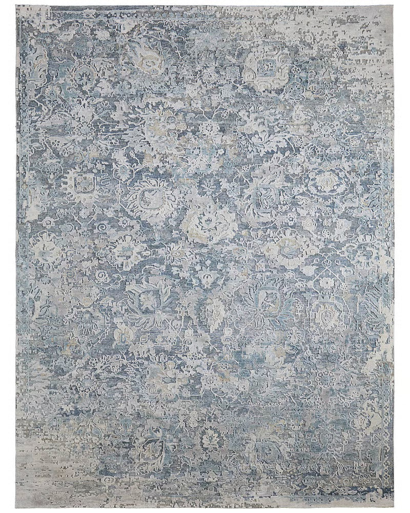 Slate blue and ivory handknotted wool and silk rug with a distressed allover floral pattern, shown corner-folded on a wood floor.