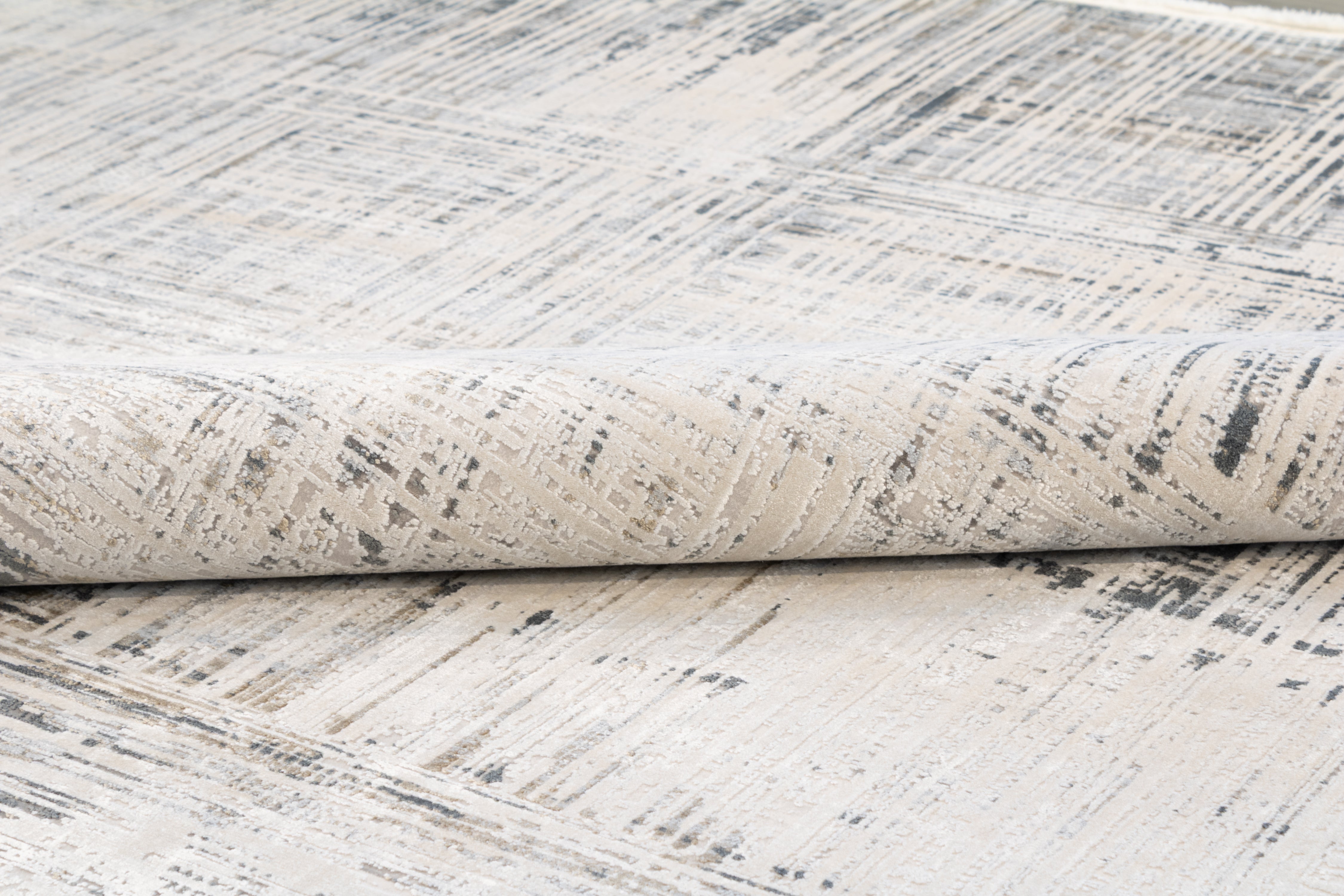 Side-angle view of the Hampton bamboo silk rug rolled tightly, showing the low pile depth, abstract surface pattern, and the flat woven underside against the face of the rug