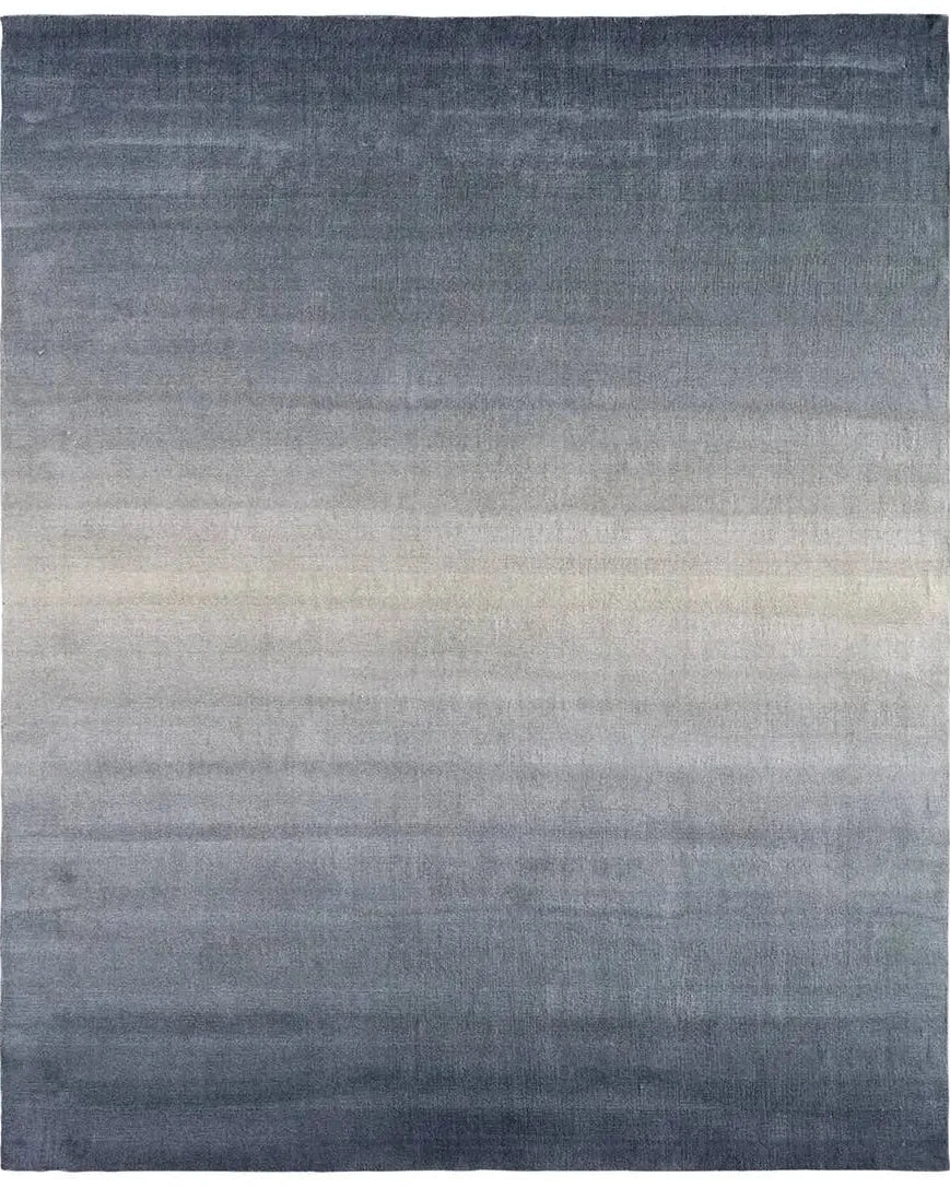 Slate blue handwoven wool rug with a soft ombré gradient fading to sand, shown in a living room setting.